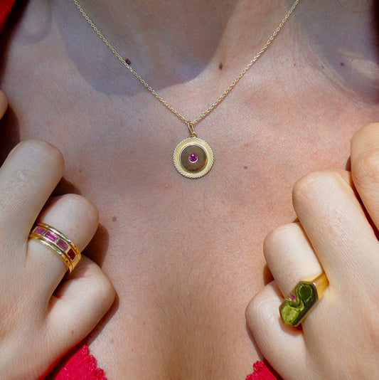 Close-up of a necklace with a circular ruby pendant and rings