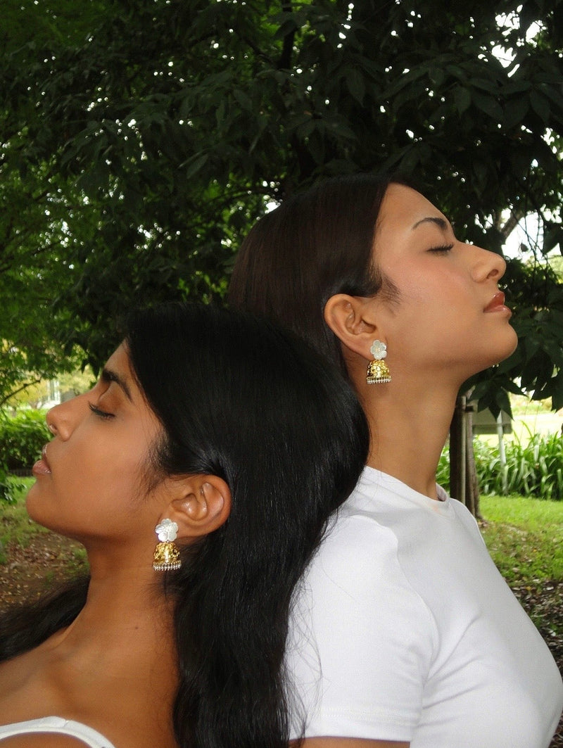 Two women standing back-to-back wearing gold plated sterling silver jhumka pearls with trees in the background 